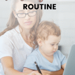A woman in glasses works at a desk while holding a young child on her lap. The text reads: How to develop a realistic work at home mom routine that actually fits your life.