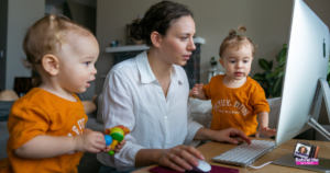 Working mom looks at her computer while her two small toddlers are right by