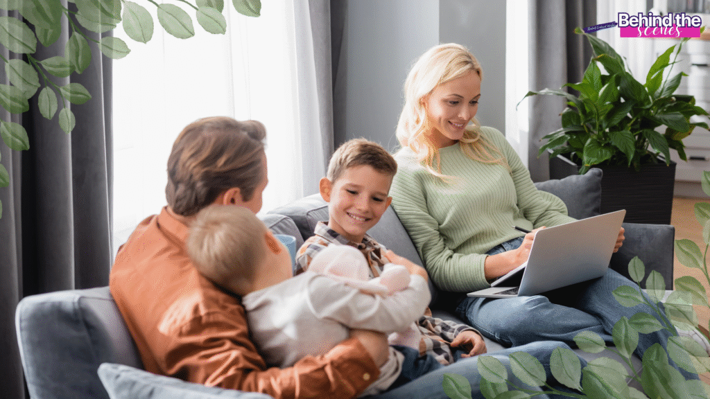 A woman sits on a couch with a laptop, smiling at two children and a man beside her. The man holds a baby, and everyone looks relaxed in a cozy, well-lit living room with leafy overlays. Behind the scenes text in the corner. Perfect example of work at home mom schedule