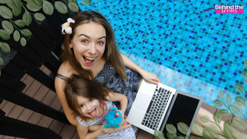 A smiling woman with a flower in her hair sits by a pool holding a laptop, with a happy young girl on her lap. Green leaves frame the scene, and Behind the scenes text appears in the corner.