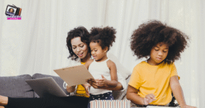 A woman sits on a couch with a laptop and clipboard, smiling at a young girl who stands beside her. Another child sits nearby, focused on writing or drawing. All three wear yellow tops. Showing work life balance for working moms