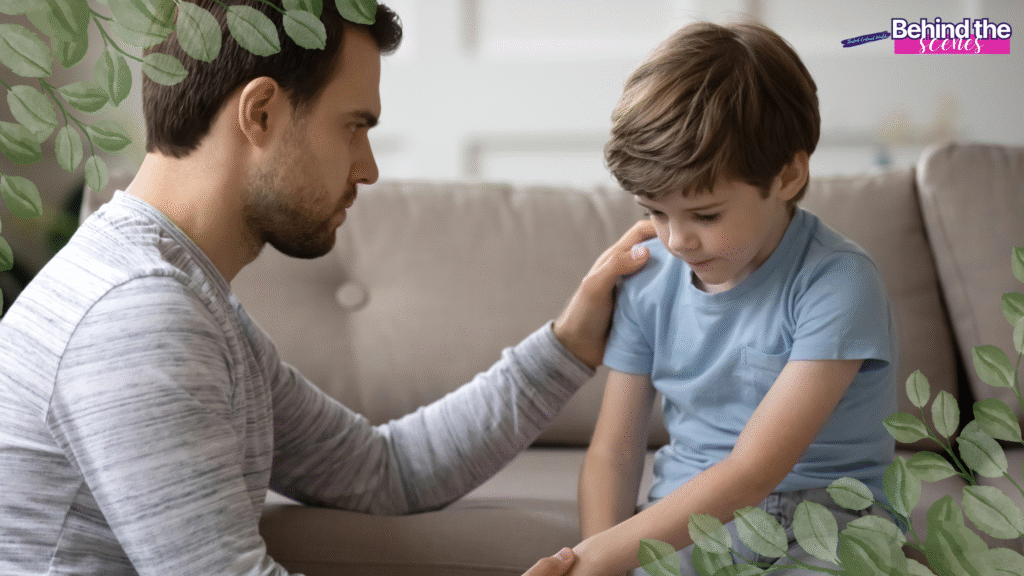 A man gently comforts a sad young boy sitting on a couch. The man has his hand on the boy’s shoulder. Green leaves partially frame the image, and a Behind the Scenes logo appears in the upper right corner. How to Talk to Kids About Scary News