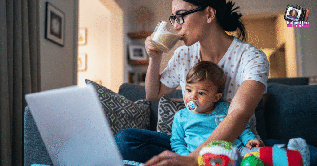 A woman sits on a couch with a baby on her lap, sipping a drink while looking at a laptop—balancing motherhood and the transition from a full-time job to entrepreneur. The cozy room features toys, a pacifier, and framed photos on the walls.
