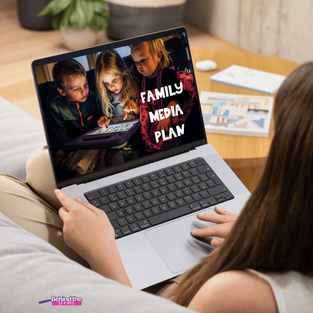 A person holds a laptop displaying an image of three children looking at a tablet, with the words FAMILY MEDIA PLAN beside them. The screen also shows a small Behind the Screen logo in the corner.