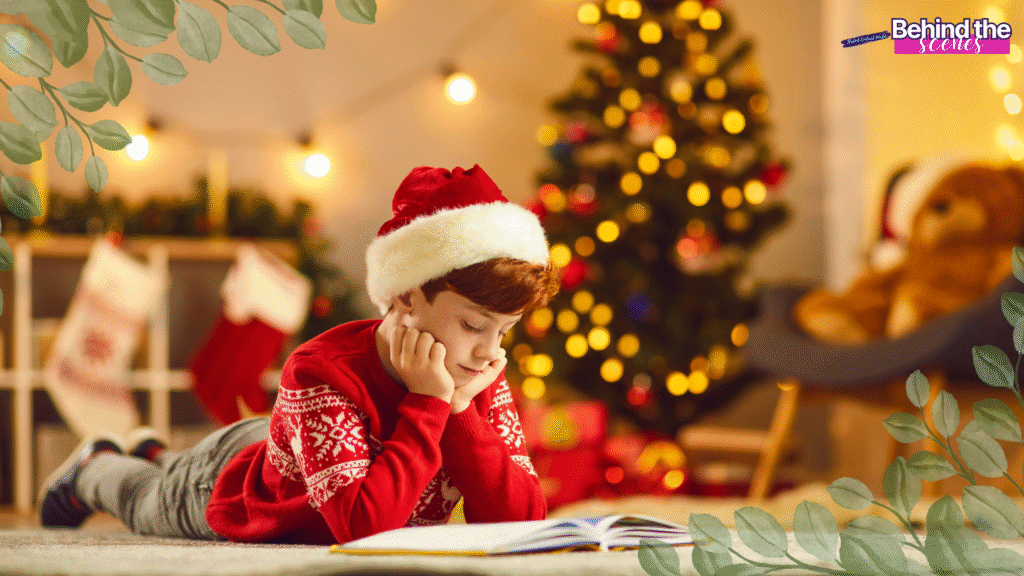 A boy in a Santa hat and red sweater lies on the floor reading a book, with a decorated Christmas tree and holiday lights in the background. Green leaves and a “Behind the scenes” label frame the image.