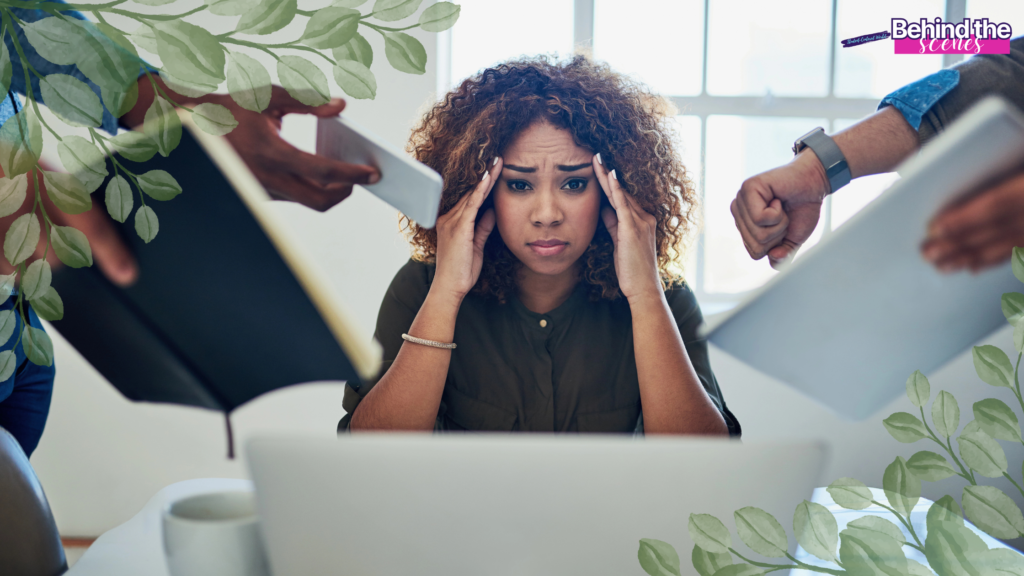 A woman sits at a desk with her hands on her temples, showing signs of career burnout. Several hands reach toward her with papers and a tablet, while plants and a Behind the scenes label frame this glimpse into career burnout recovery.