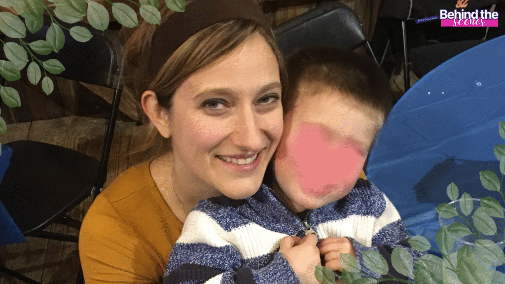 A smiling woman hugs a young child in a striped sweater at an indoor event. The childs face is blurred. There are leafy decorations on the corners, and Behind the Scenes text is in the top right corner.