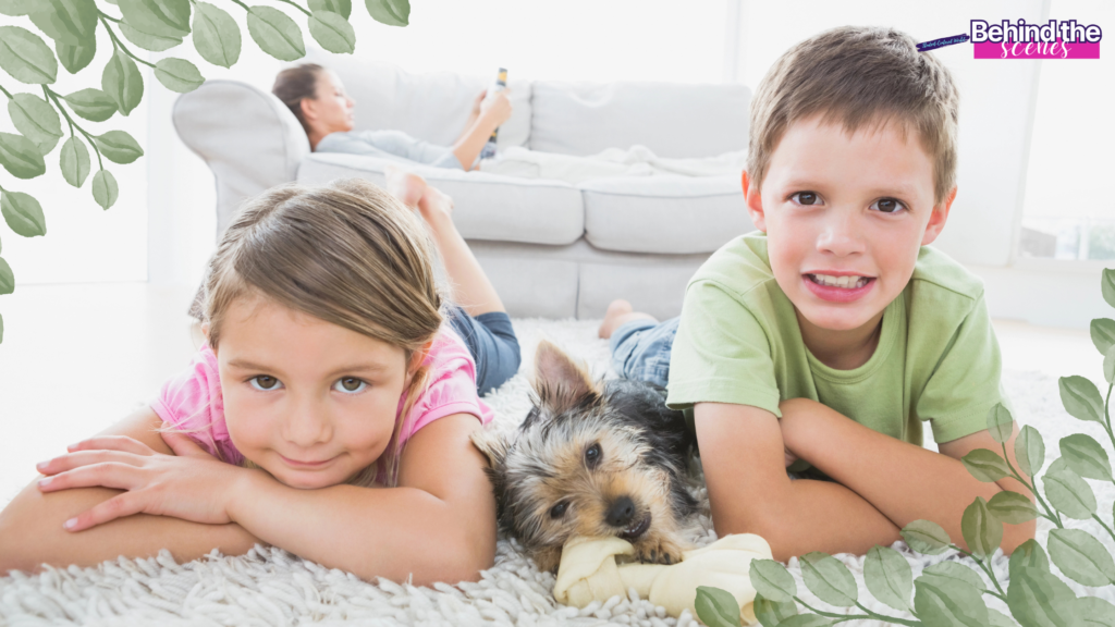 Two young children lie on a rug next to a small dog, smiling at the camera. In the background, an adult relaxes on a sofa with a phone. Green leafy borders and Behind the Scenes text highlight how to make home feel safe and cozy. 