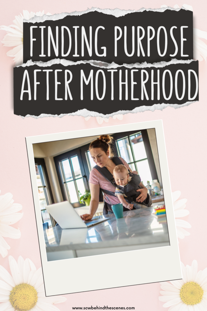 A mother stands in a kitchen, holding a baby in a carrier while working on a laptop. Text above reads Finding Purpose After Motherhood. White daisies decorate the pink background.